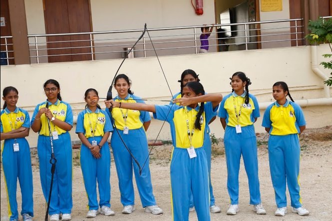 Students in sports uniform practising archery on the school ground